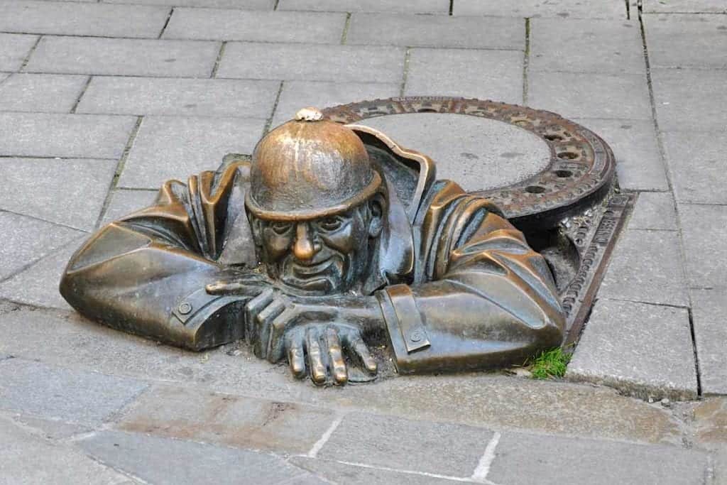 Bratislava Bronze Cumil statue peering out of manhole cover.