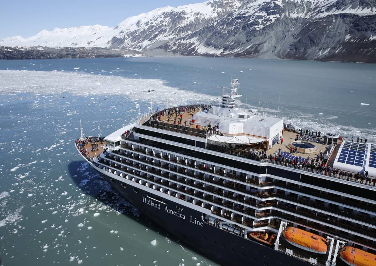 Holland America Line cruise ship sailing in Alaska with a snow covered mountain and icy ocean in the background.