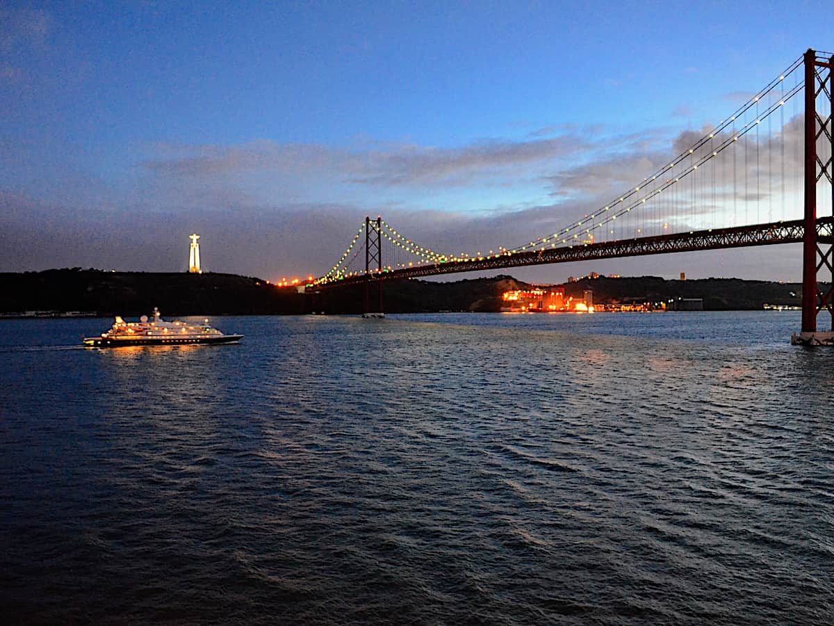 Leaving Lisbon after sunset with suspension bridge lights lit.